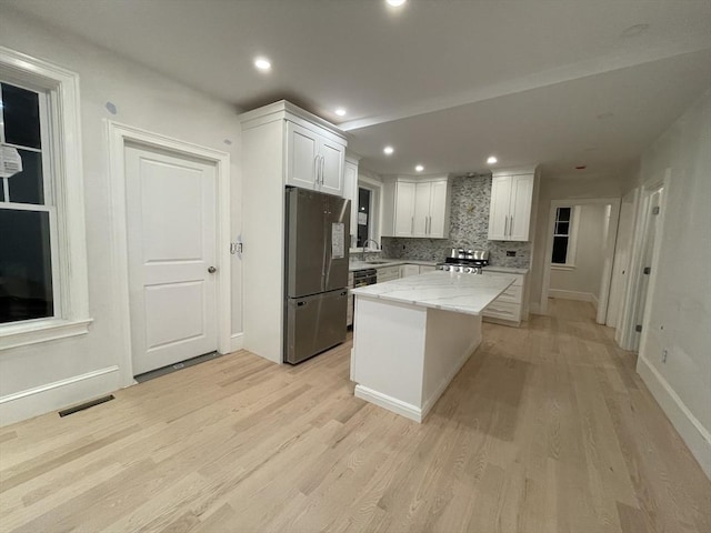 kitchen featuring white cabinetry, stainless steel appliances, decorative backsplash, a kitchen island, and light wood-type flooring