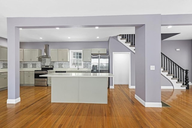 kitchen featuring decorative backsplash, wall chimney range hood, a kitchen island, stainless steel appliances, and gray cabinets