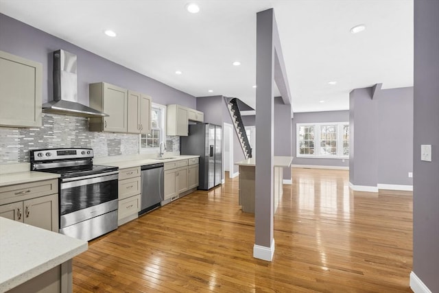 kitchen featuring wall chimney range hood, stainless steel appliances, tasteful backsplash, sink, and light wood-type flooring