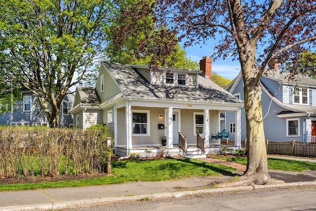 bungalow-style home with covered porch, fence, a shingled roof, and a chimney
