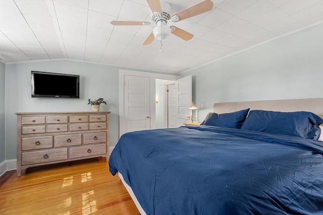 bedroom with crown molding, baseboards, ceiling fan, light wood-style floors, and lofted ceiling