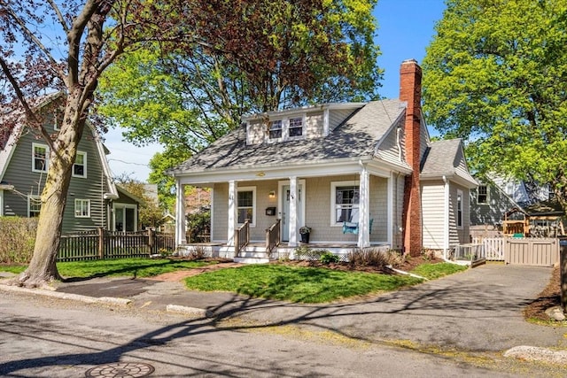 bungalow-style home featuring a porch, roof with shingles, a chimney, and fence
