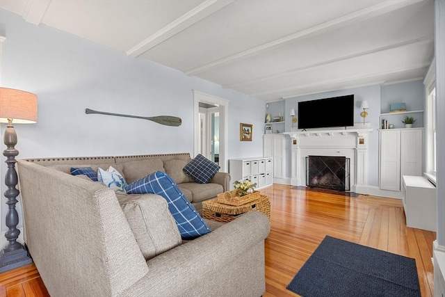 living area featuring beamed ceiling, a fireplace with flush hearth, and wood finished floors