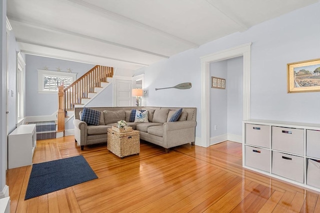 living room featuring light wood-style floors, stairway, baseboards, and beam ceiling