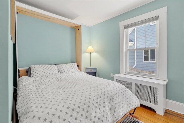 bedroom with ornamental molding, radiator, baseboards, and wood finished floors