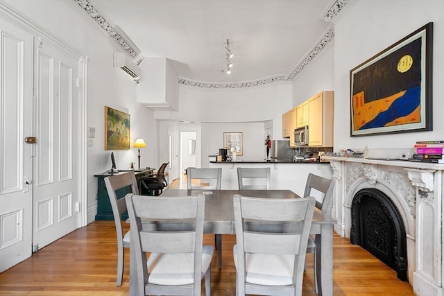 dining space with an AC wall unit, crown molding, a high end fireplace, and light wood-type flooring