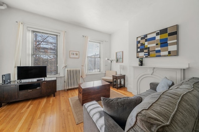 living room with a fireplace, radiator heating unit, a healthy amount of sunlight, and light hardwood / wood-style flooring