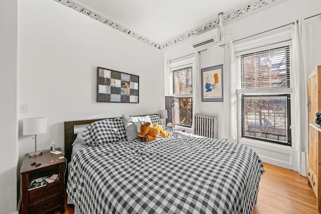 bedroom featuring a wall mounted air conditioner, radiator heating unit, light wood-type flooring, and multiple windows