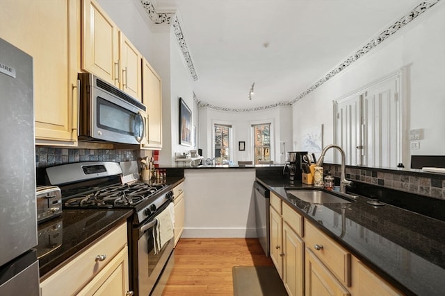 kitchen featuring sink, stainless steel appliances, kitchen peninsula, dark stone countertops, and light hardwood / wood-style floors