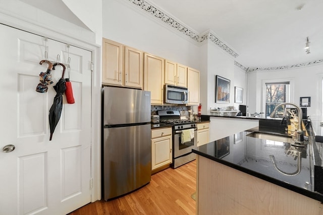 kitchen featuring sink, dark stone countertops, light wood-type flooring, appliances with stainless steel finishes, and kitchen peninsula