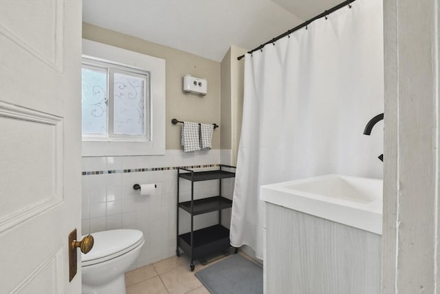 bathroom with tile patterned flooring, lofted ceiling, toilet, vanity, and tile walls