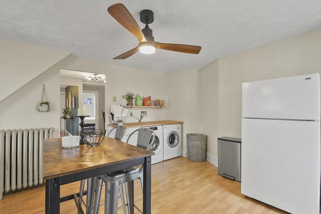 interior space with ceiling fan, radiator heating unit, washing machine and dryer, white refrigerator, and light wood-type flooring