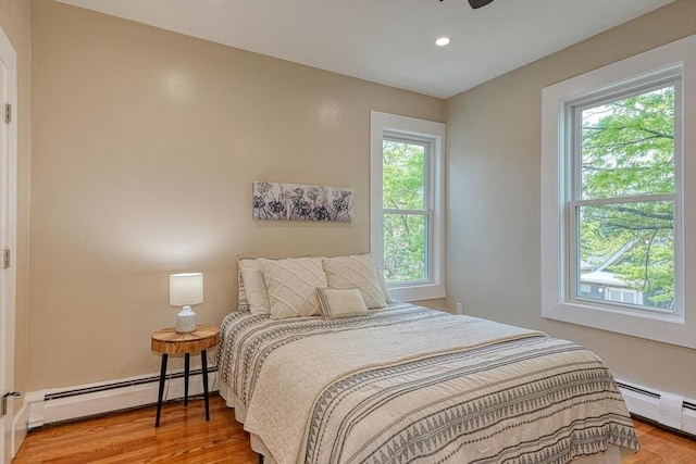 bedroom with a baseboard heating unit, wood finished floors, and recessed lighting
