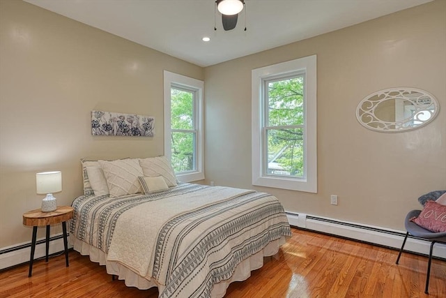 bedroom featuring a baseboard radiator, multiple windows, and wood finished floors