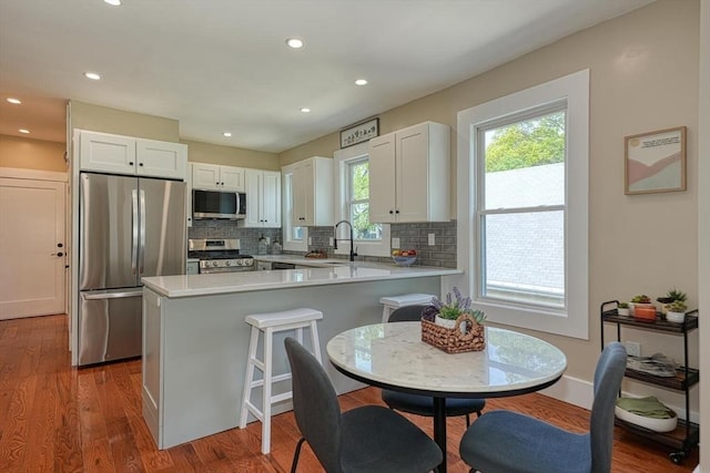 kitchen with appliances with stainless steel finishes, white cabinetry, a peninsula, tasteful backsplash, and recessed lighting