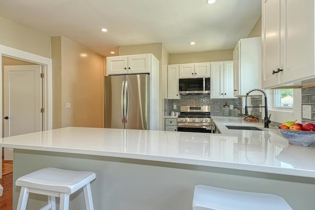 kitchen featuring appliances with stainless steel finishes, a sink, tasteful backsplash, a peninsula, and white cabinets