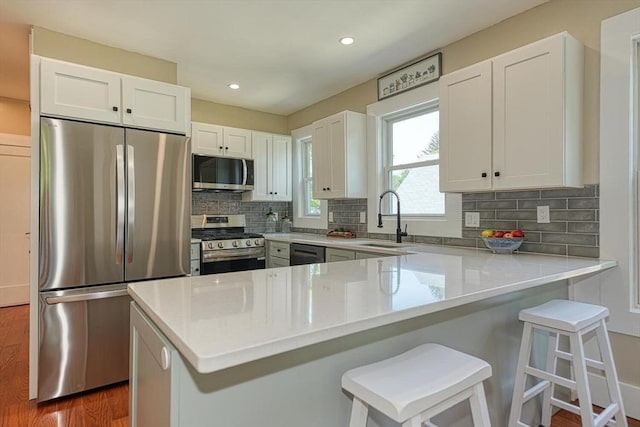 kitchen with stainless steel appliances, a sink, a peninsula, wood finished floors, and tasteful backsplash