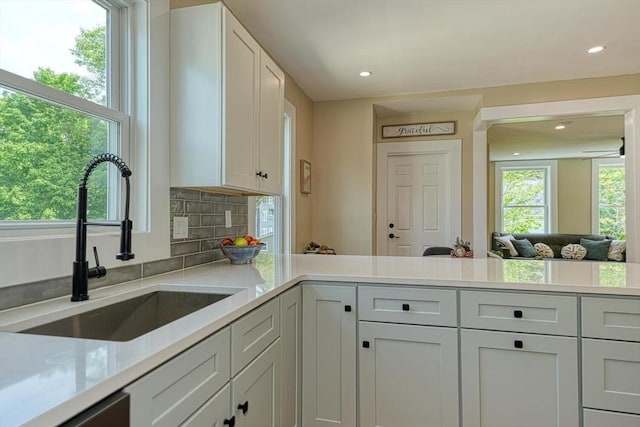 kitchen with a sink, recessed lighting, backsplash, white cabinets, and a peninsula