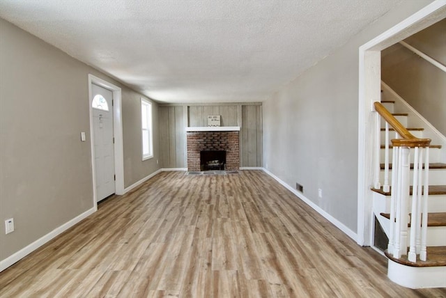 unfurnished living room with a brick fireplace, light hardwood / wood-style floors, and a textured ceiling