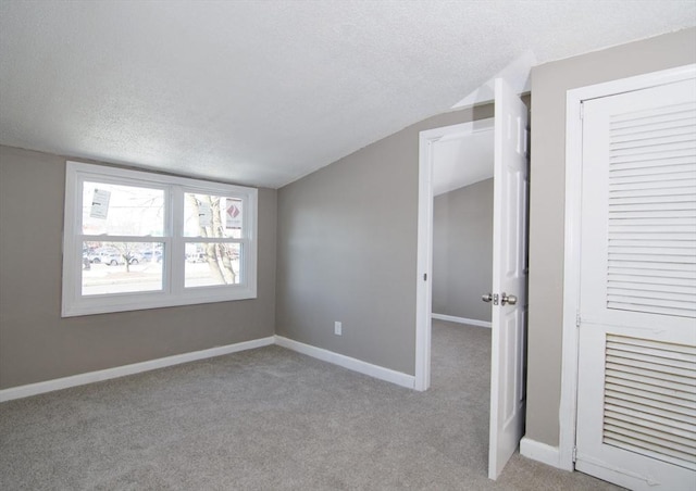 unfurnished room with vaulted ceiling, light carpet, and a textured ceiling