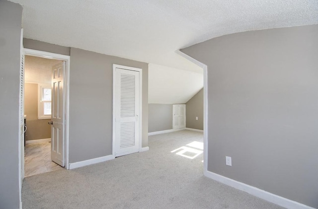 bonus room with lofted ceiling, light carpet, and a textured ceiling