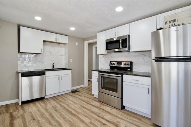 kitchen with appliances with stainless steel finishes, sink, white cabinets, and light hardwood / wood-style flooring