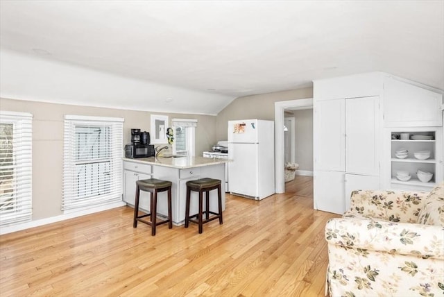 kitchen featuring a breakfast bar area, a sink, light wood-style floors, freestanding refrigerator, and a peninsula