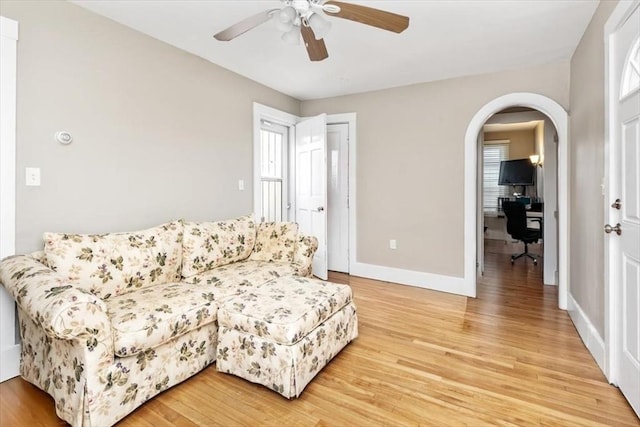 living area featuring arched walkways, baseboards, light wood finished floors, and ceiling fan