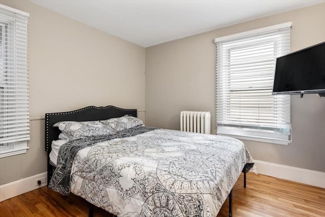 bedroom featuring multiple windows, wood finished floors, radiator heating unit, and baseboards