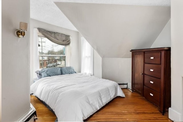 bedroom with lofted ceiling, wood finished floors, a baseboard heating unit, and a textured ceiling