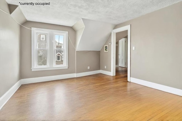 bonus room featuring a textured ceiling, baseboards, vaulted ceiling, and wood finished floors