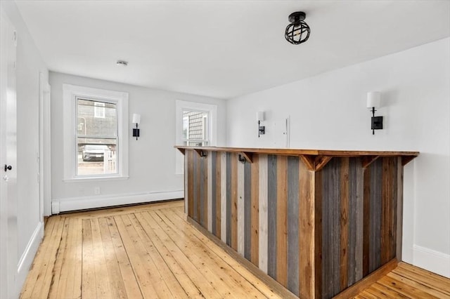 bar featuring a bar, baseboards, baseboard heating, and light wood-type flooring