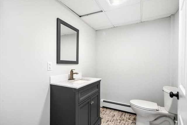 bathroom featuring toilet, wood finished floors, vanity, baseboard heating, and a paneled ceiling