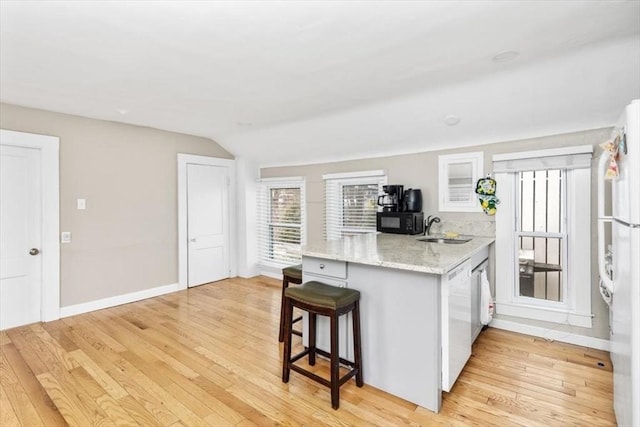 kitchen with a peninsula, a kitchen bar, black microwave, a sink, and light wood-type flooring