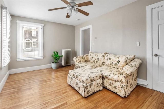 living area with baseboards, ceiling fan, light wood-style flooring, and radiator heating unit