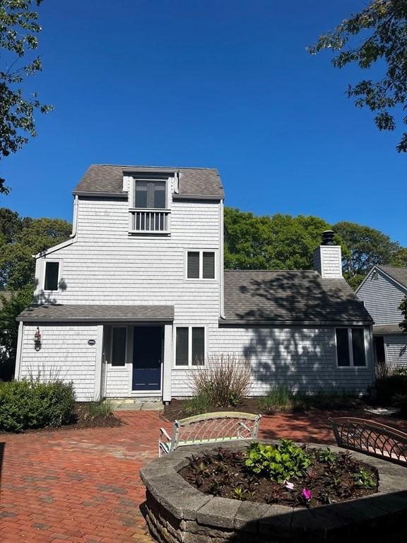 view of front facade featuring roof with shingles, a patio, and a chimney