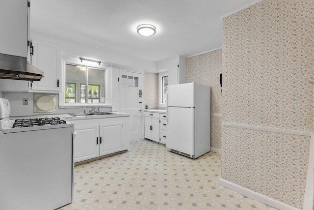kitchen featuring white appliances, wallpapered walls, a sink, healthy amount of natural light, and white cabinets
