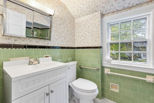 bathroom featuring wallpapered walls, tile walls, vaulted ceiling, toilet, and healthy amount of natural light