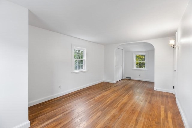 unfurnished room featuring arched walkways, light wood-style flooring, and baseboards