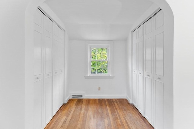 unfurnished bedroom with light wood finished floors, baseboards, arched walkways, and two closets