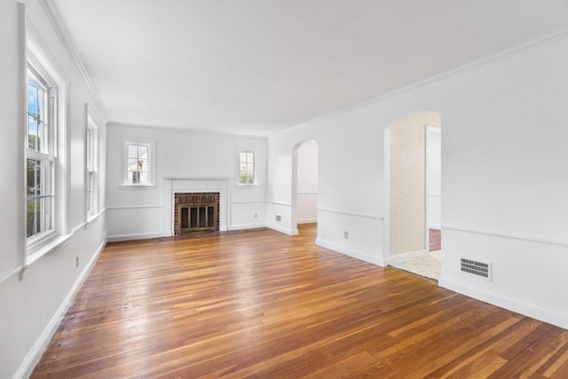 unfurnished living room featuring arched walkways, wood finished floors, a brick fireplace, ornamental molding, and baseboards