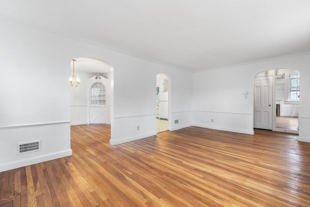 unfurnished living room featuring arched walkways, light wood-style flooring, ornamental molding, baseboards, and a chandelier