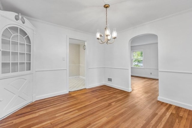 unfurnished dining area featuring arched walkways, light wood-type flooring, a chandelier, crown molding, and baseboards