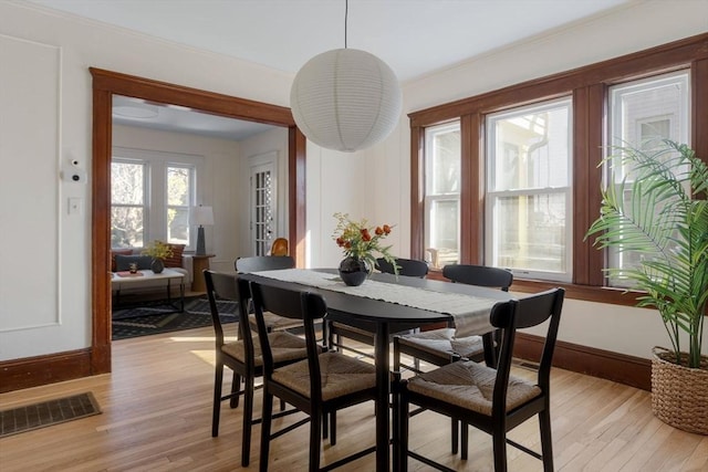 dining room with ornamental molding, light wood finished floors, visible vents, and baseboards