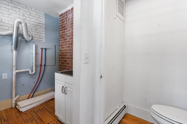 bathroom featuring toilet, brick wall, a baseboard heating unit, and wood finished floors