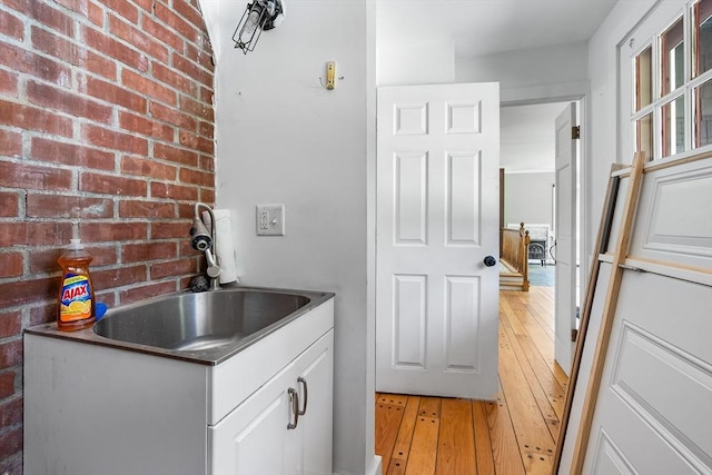 laundry area featuring a sink, brick wall, and light wood-style flooring