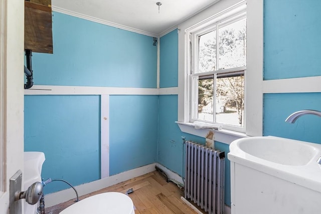bathroom with crown molding, a sink, toilet, radiator heating unit, and wood finished floors