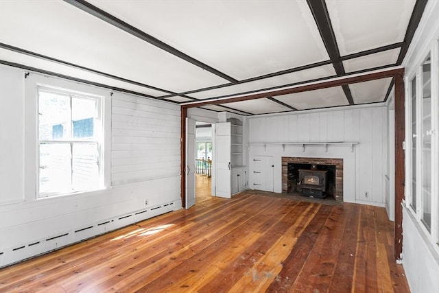 unfurnished living room with a baseboard radiator, a wood stove, wooden walls, and hardwood / wood-style flooring