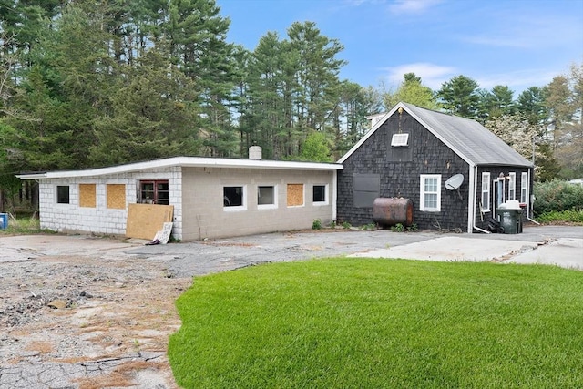 view of front of house featuring concrete block siding, heating fuel, a chimney, and a front lawn
