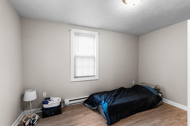 bedroom with baseboards, baseboard heating, and wood finished floors